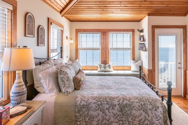 Bright living room with beige sofa, blue patterned rug, ceiling fan, glass doors opening to deck, and wall-mounted TV.